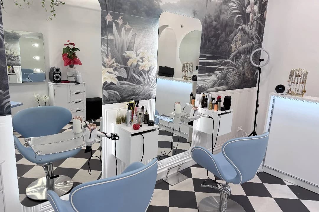 Le postazioni del salone: poltrone azzurre, specchi a tutta altezza e carta da parati tropicale in bianco e nero